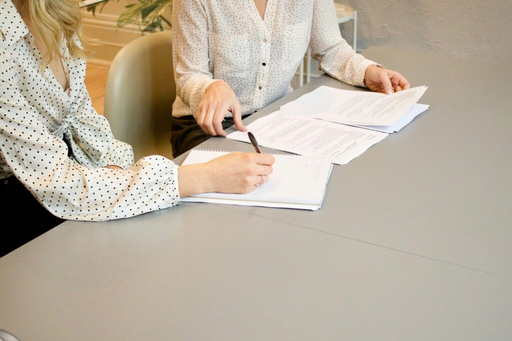 Woman signing documents beside another woman