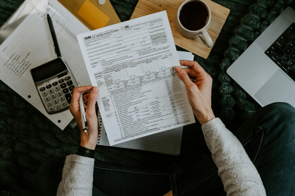 Hands holding tax forms with a calculator and laptop